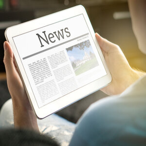 Male sitting outside in the sunshine, reading news on a tablet.